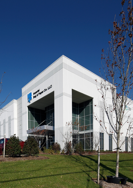 A white industrial building with a blue and black sign in front.